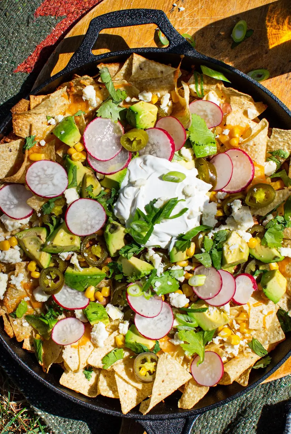 loaded campfire nachos in a cast iron skillet topped with corn, chunks of avocado, radish slices, sour cream, crumbled cheese, and cilantro