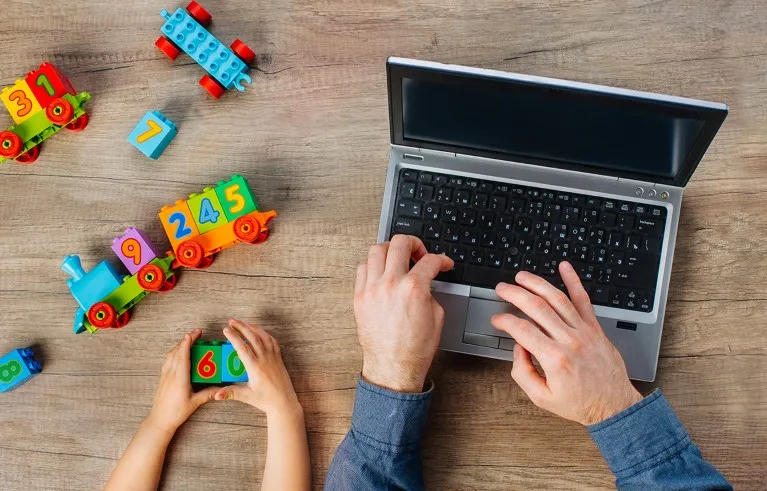 Close up of kids hands playing with colorful blocks near father working on the laptop. Work from home during quarantine concept. Top view, flat lay.