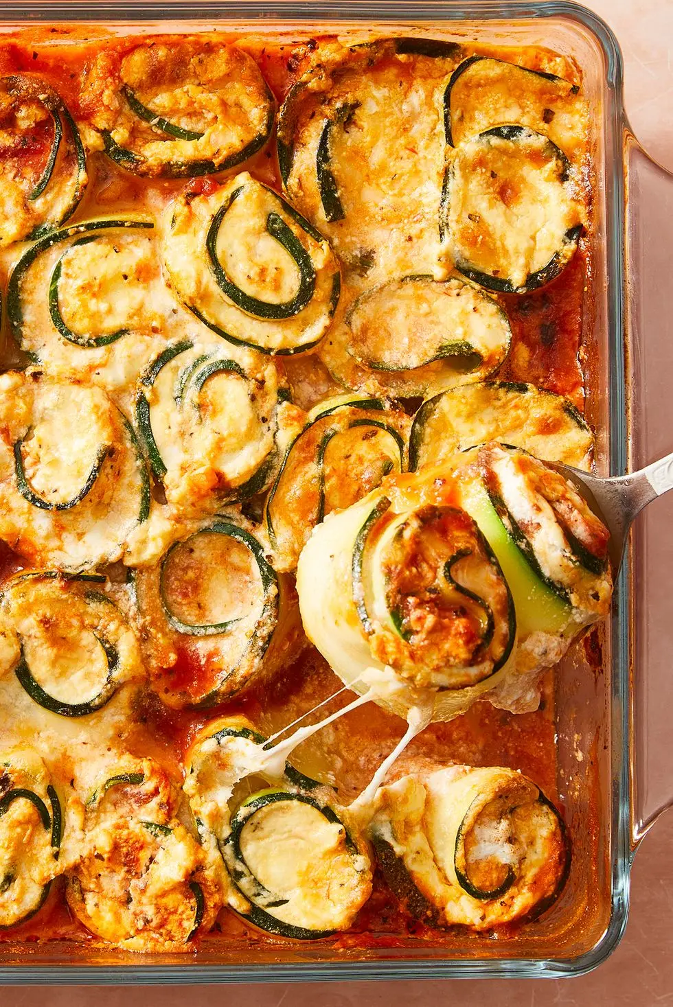 zucchini slices rolled up around cheese with sauce in a casserole dish