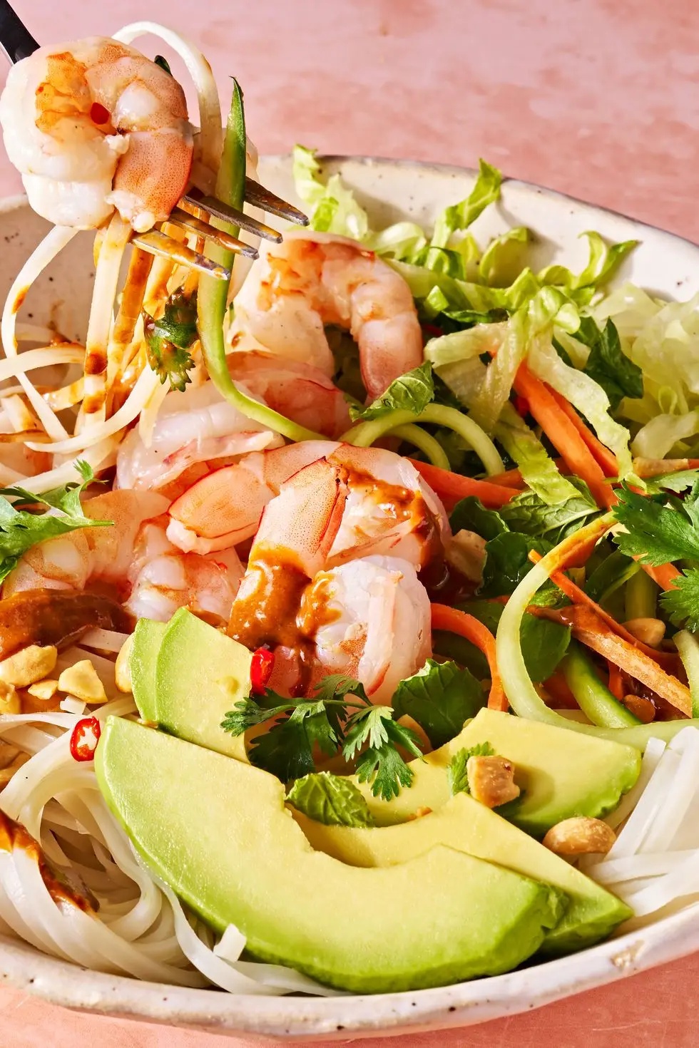 fork lifting a bite of summer roll bowl with rice noodles, shrimp, avocado, and peanuts