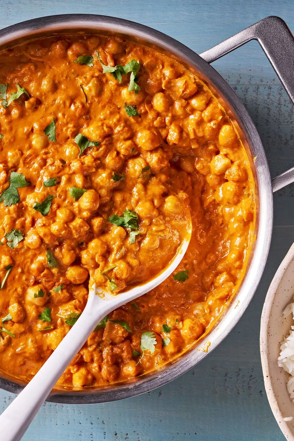 indian butter chickpeas in a pan with a bowl of rice on the side