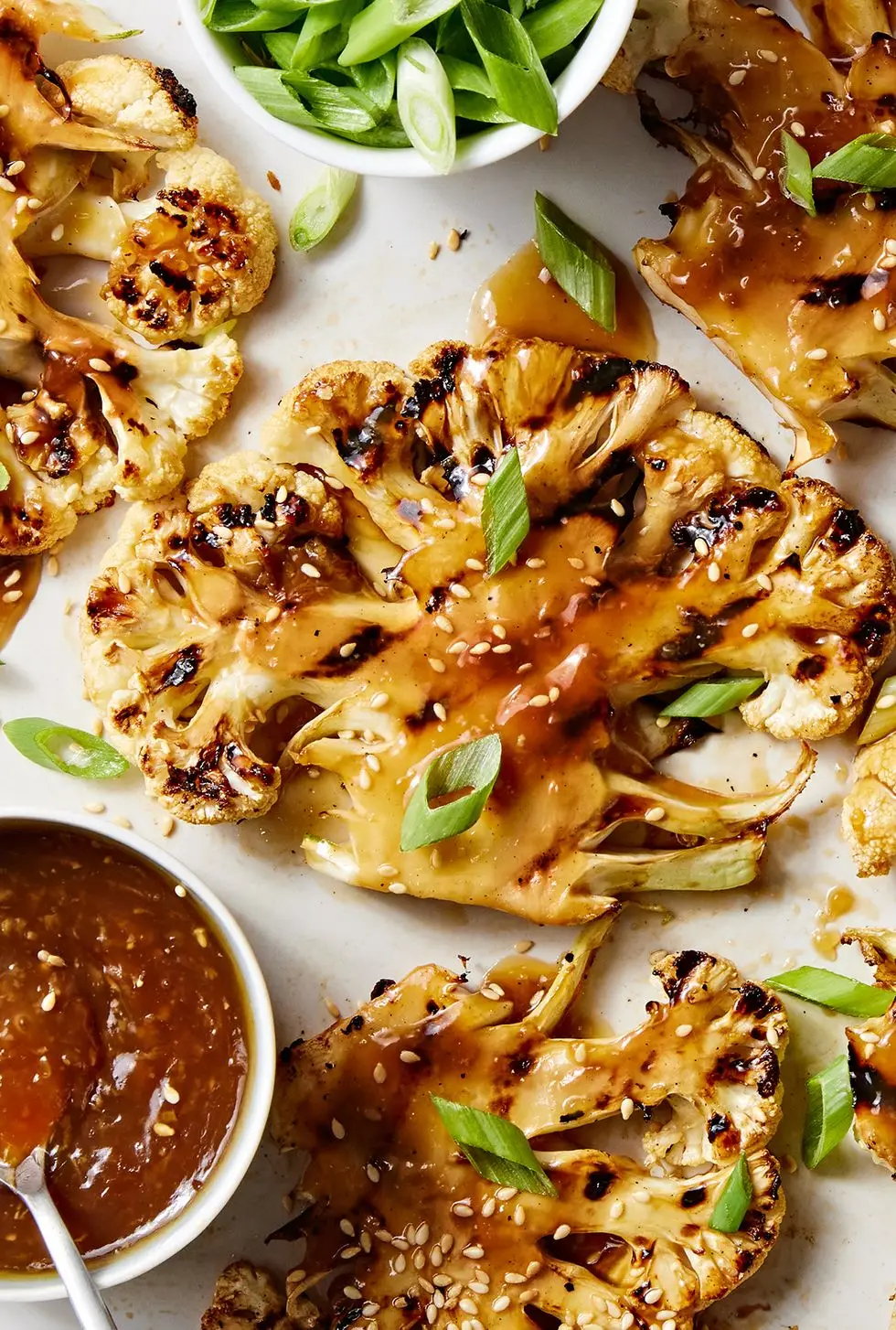 grilled teriyaki cauliflower steaks on a platter with more teriyaki sauce and scallions