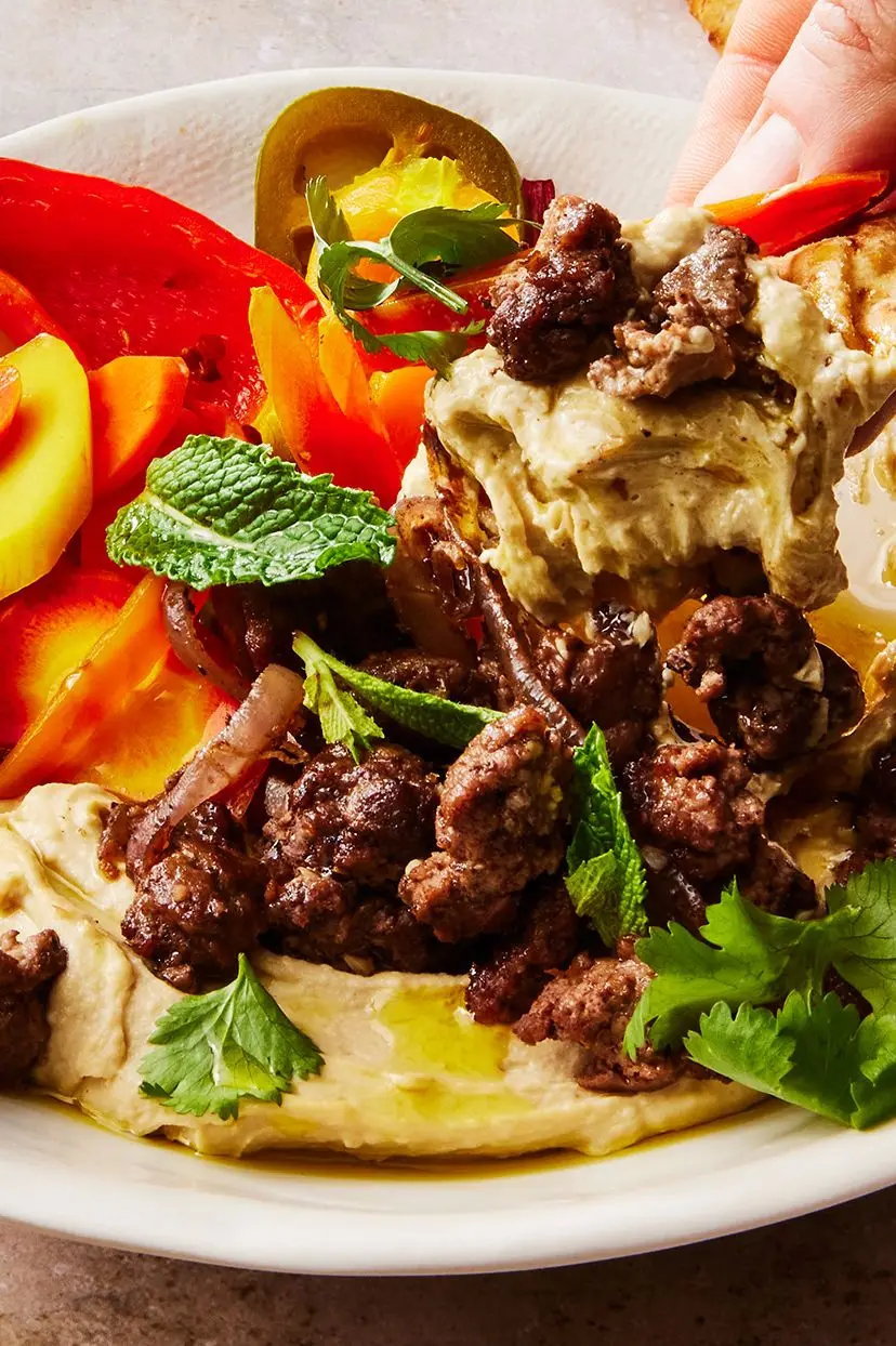 hummus bowl topped with spiced lamb, homemade pickled vegetables, and herbs