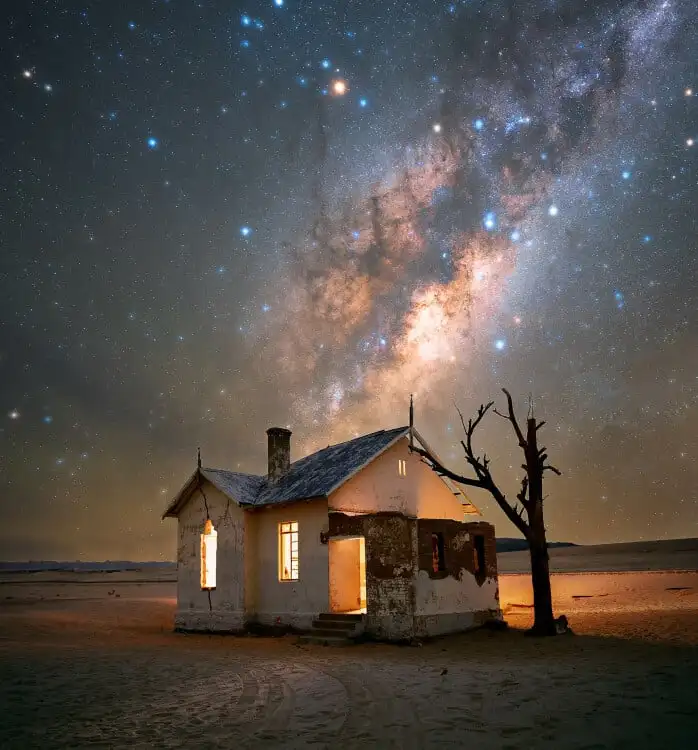 This image shows an abandoned house in the middle of the Namib Desert with the Milky Way rising above it.