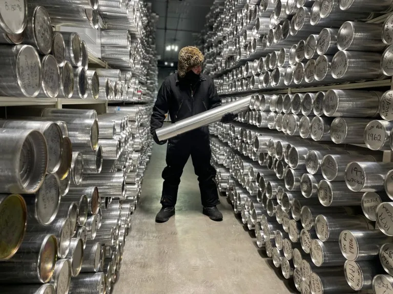 A man wearing a hat and warm clothing inserts a silver cylinder into a huge rack of similar containers.