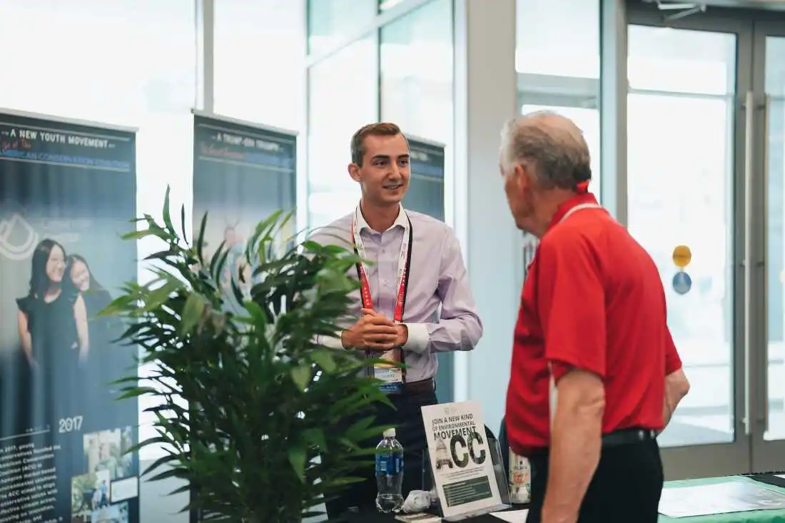 Aidan Shank talking to a guest at the ACC Exhibition booth in Baird Center.