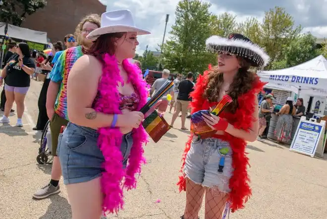 Decked out in cowgirl hats and feather boas, friends Haley Dunn, left, of Germantown Hills and Sammi Williams of Metamora chat as they wait in line for refreshments during the annual River City Pride Festival on Saturday, July 20, 2024 on the Peoria riverfront.