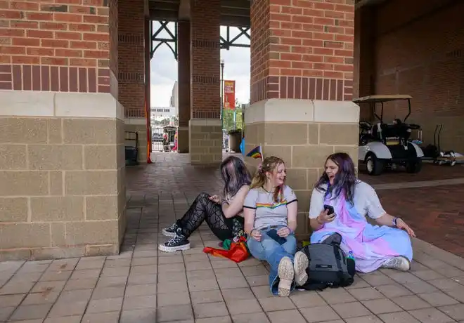 Charlie, right, and Oscar, middle, share a laugh as Oscar’s partner Naeveh scans her cellphone during a quiet moment under the Gateway Building on Saturday, July 20, 2024 at the River City Pride Festival on the Peoria riverfront.