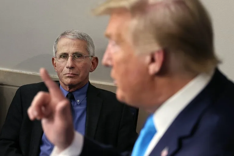 Anthony Fauci (background, in focus) listens to a speech by Donald Trump (foreground, blurred).