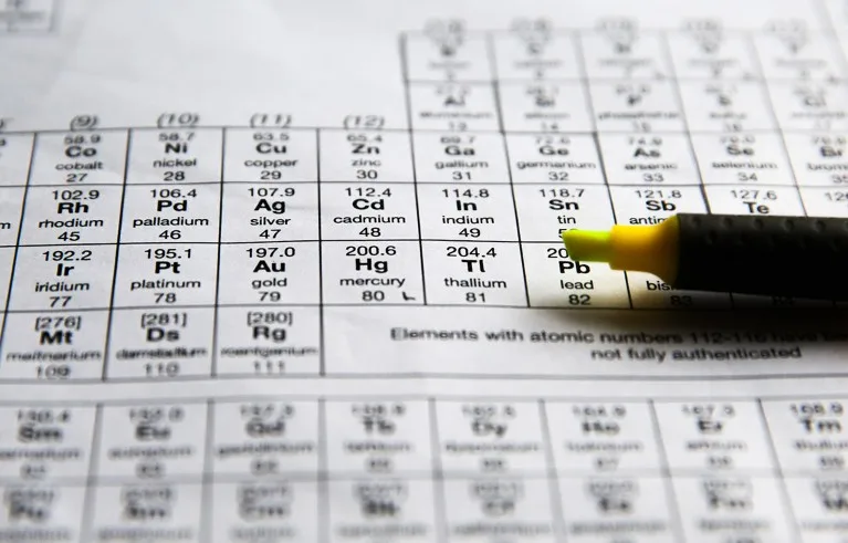 Close up view of a yellow highlighter pen resting atop a printed paper copy of the periodic table.