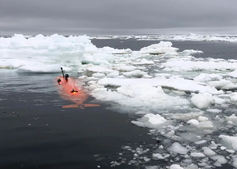 An orange submersible sits just below the surface of icy water on a cloudy day