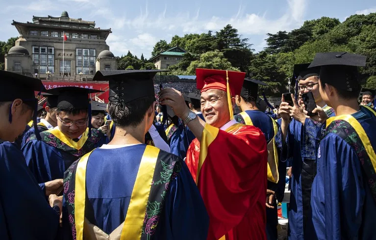 Dressed in red robes, Dou Xiankang adjusts a graduate's tassel during their graduations ceremony at Wuhan University.