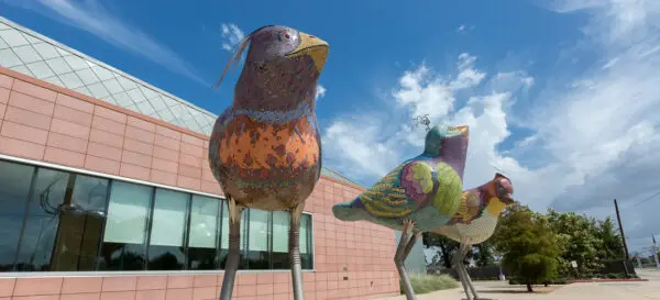 A photograph of a public art sculpture featuring three large birds covered in mosaic tiles.