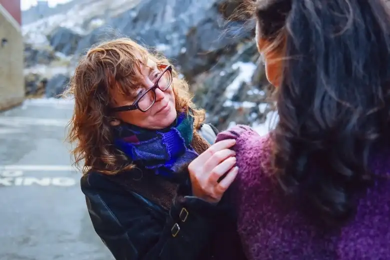 Woman with curly hair and glasses pinning a piece of fabric to someone's shoudler.