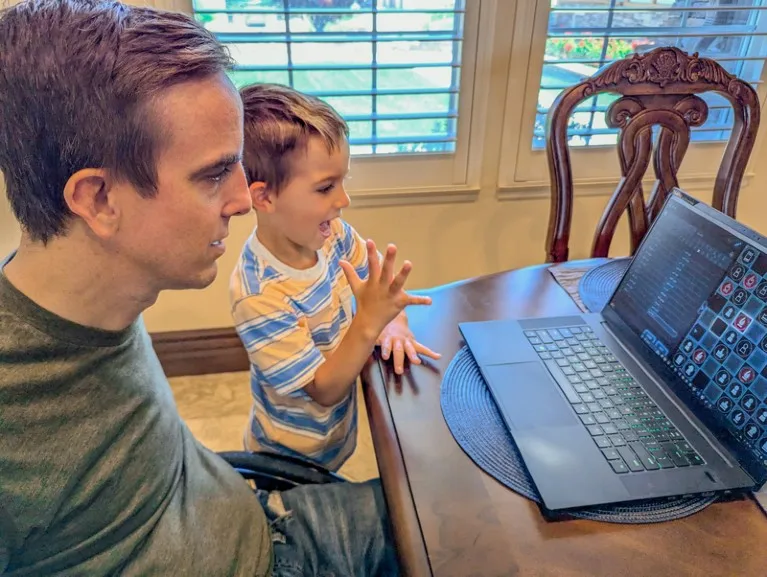 Chris Cantwell and his young son sit at a dining table playing Quantum Chess on a laptop computer