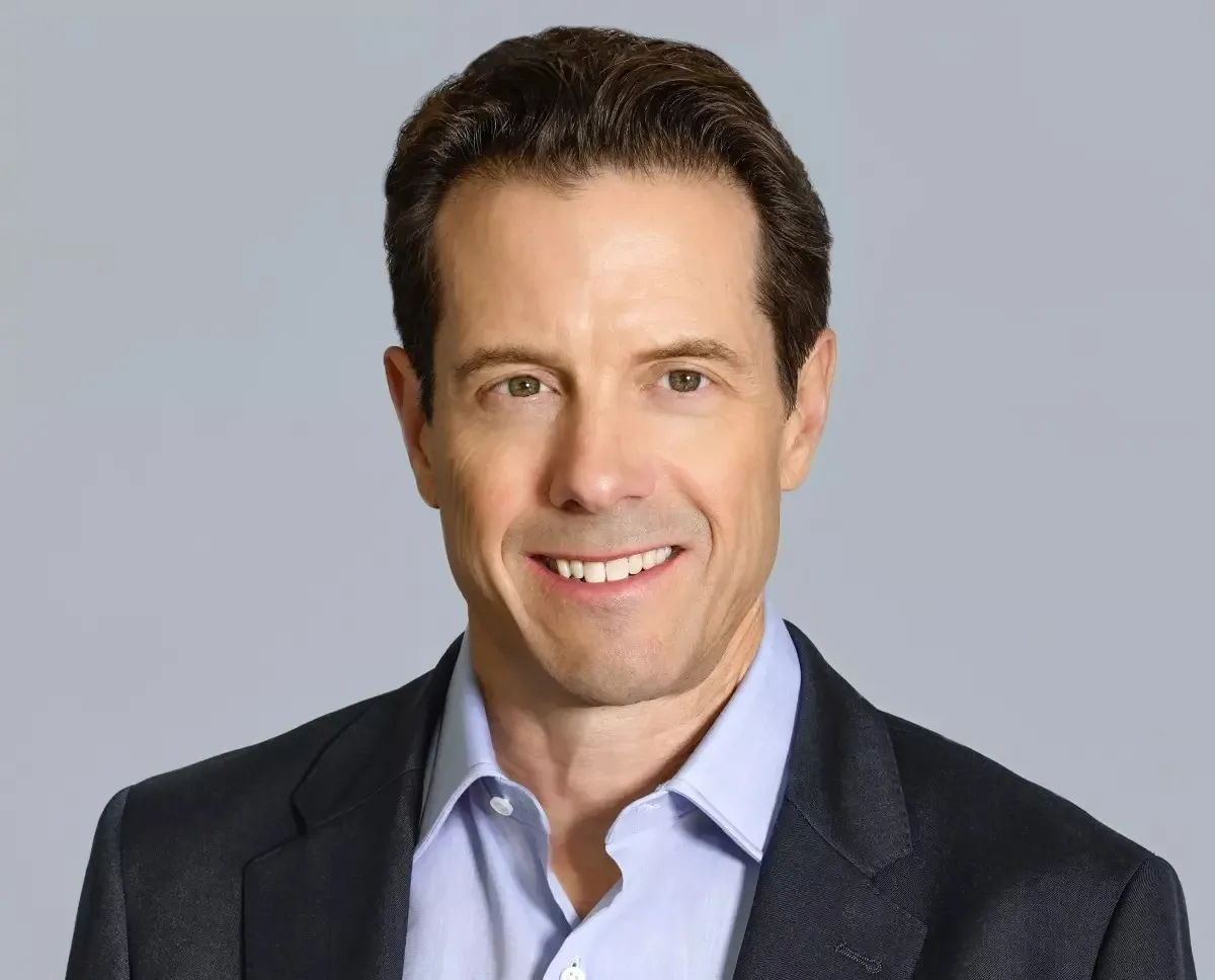 A man with short brown hair, wearing a light blue button-up shirt and dark blazer, smiles against a plain grey background, reminiscent of a modern-day Disney executive.