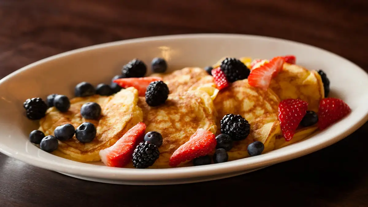 A plate of small pancakes topped with berries and syrup.