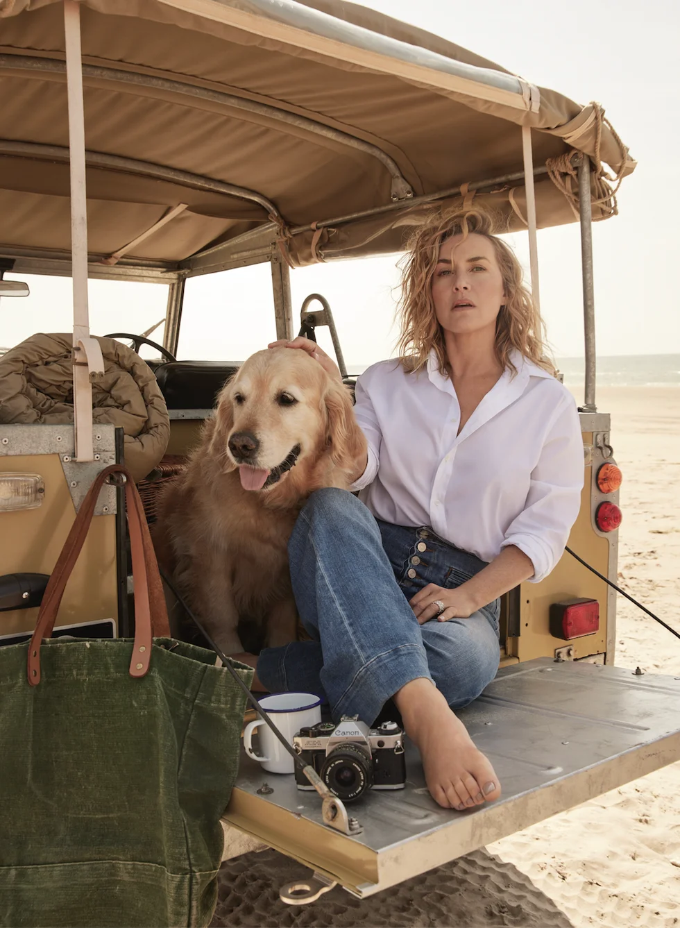 kate winslet sits at the back of a van with a camera and a dog