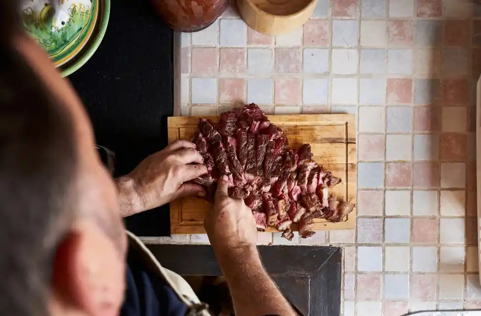 high view of tomakawk steak on cutting board in a kitchen and man preparing tomakawk steak on a kitchen counter food and drink concept