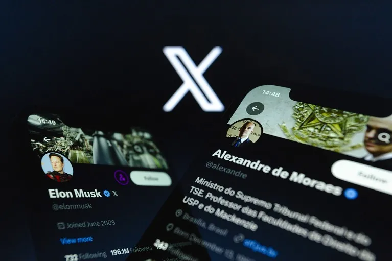 Elon Musk and Alexandre de Moraes accounts on X displayed on two smartphones backdropped by the X logo.