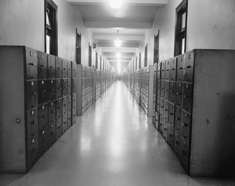 A black and white photograph of a hallway lined with old filing cabinets