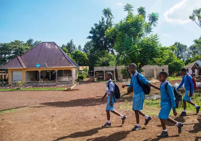 Children in blue school uniforms walk along an unpaved road In Tanzania