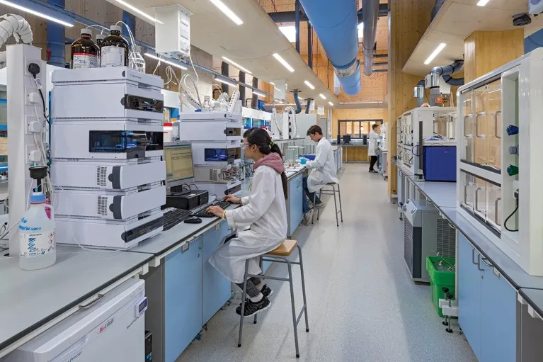 Science lab with wooden walls. White-coated researchers are working at benches.