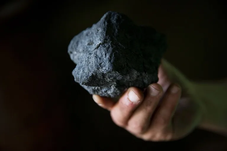 Close up view of a hand holding a lump of coal.