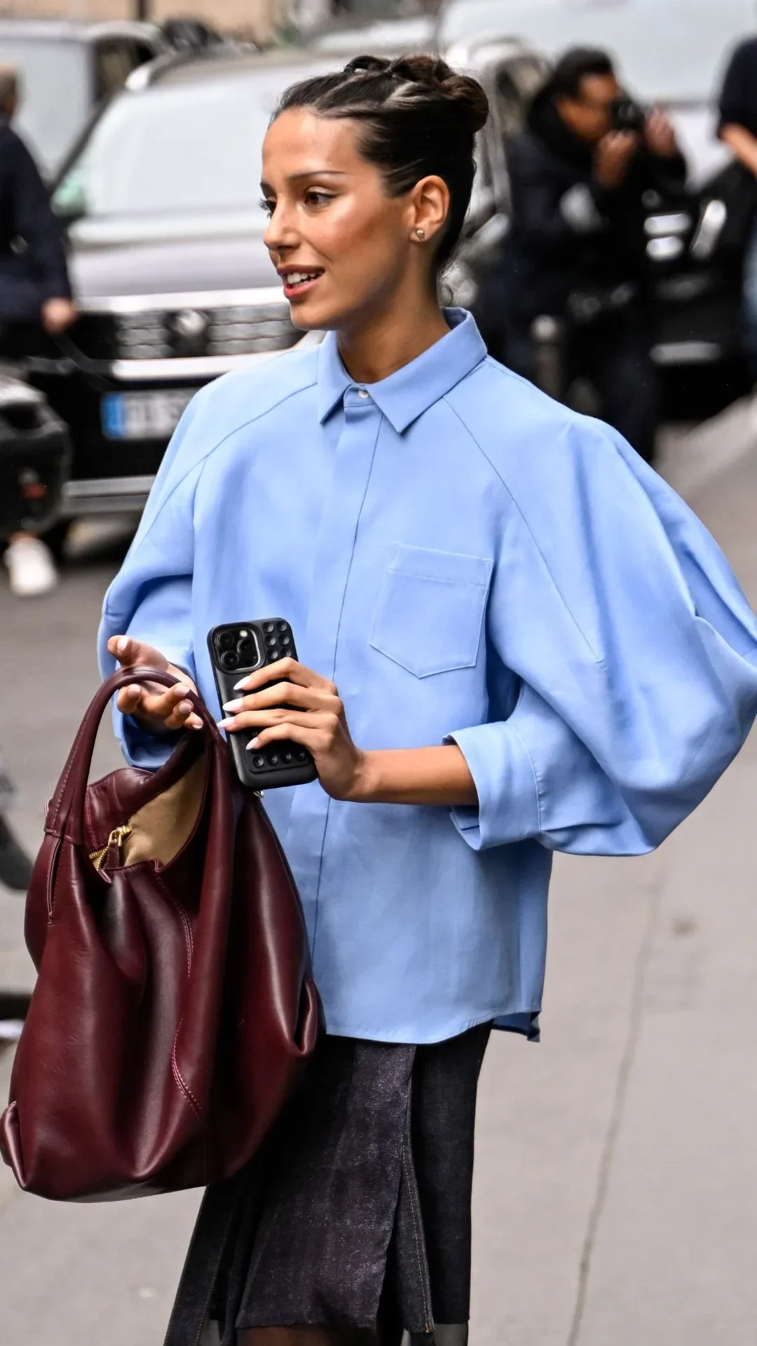 A guest is seen wearing a blue Sacai shirt, Sacai skirt and burgundy bag outside the Gabriela Hearst show during Womenswear Spring/Summer 2025 as part of Paris Fashion Week on September 30, 2024 in Paris, France. 