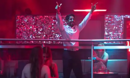 A man standing in a nightclub with both arms raised.