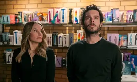 A man and a woman stand next to each other in front of shelves displaying sex toys.