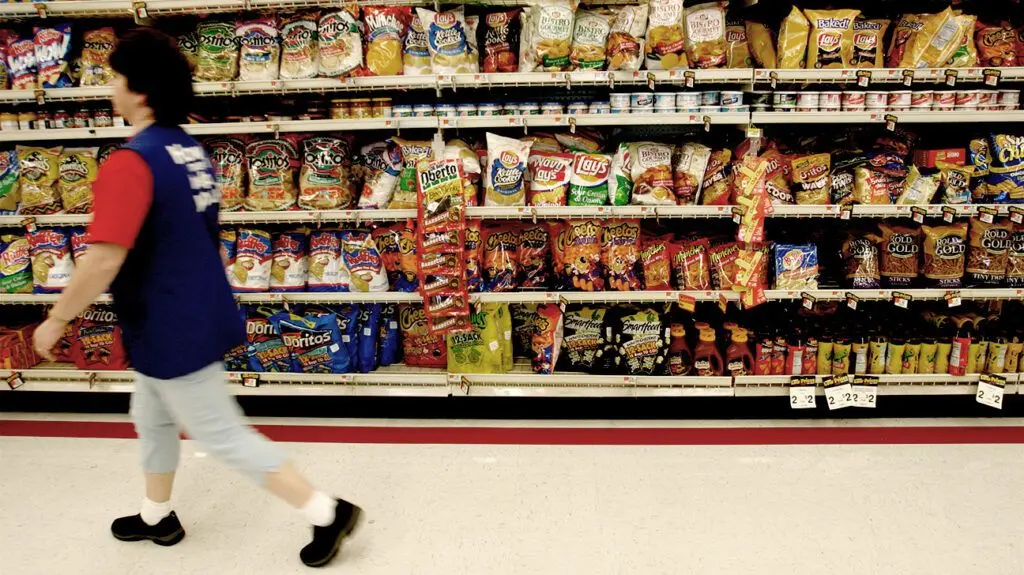 person walking by supermarket snack shelves