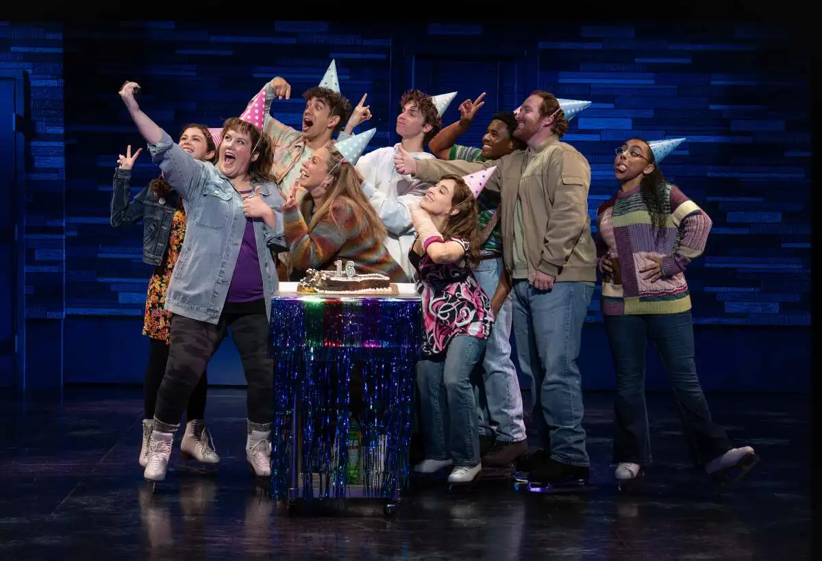 A group of people onstage pose for a selfie at a birthday party