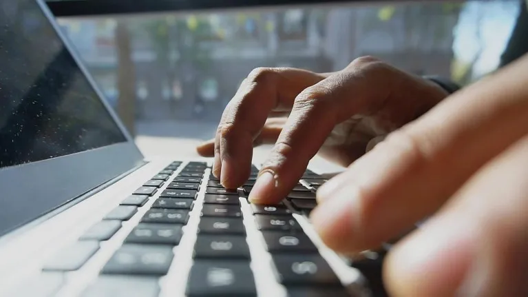 Close up view of a man's hands type words on a laptop keyboard.