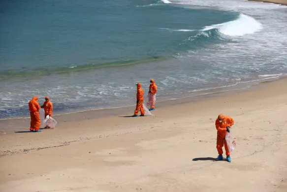 Council workers in hazmat suits cleaning tar balls off Coogee Beach.