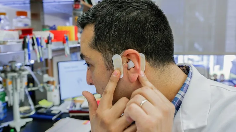 A researcher demonstrates how to attach a device named the neural tourniquet to the skin over the ear