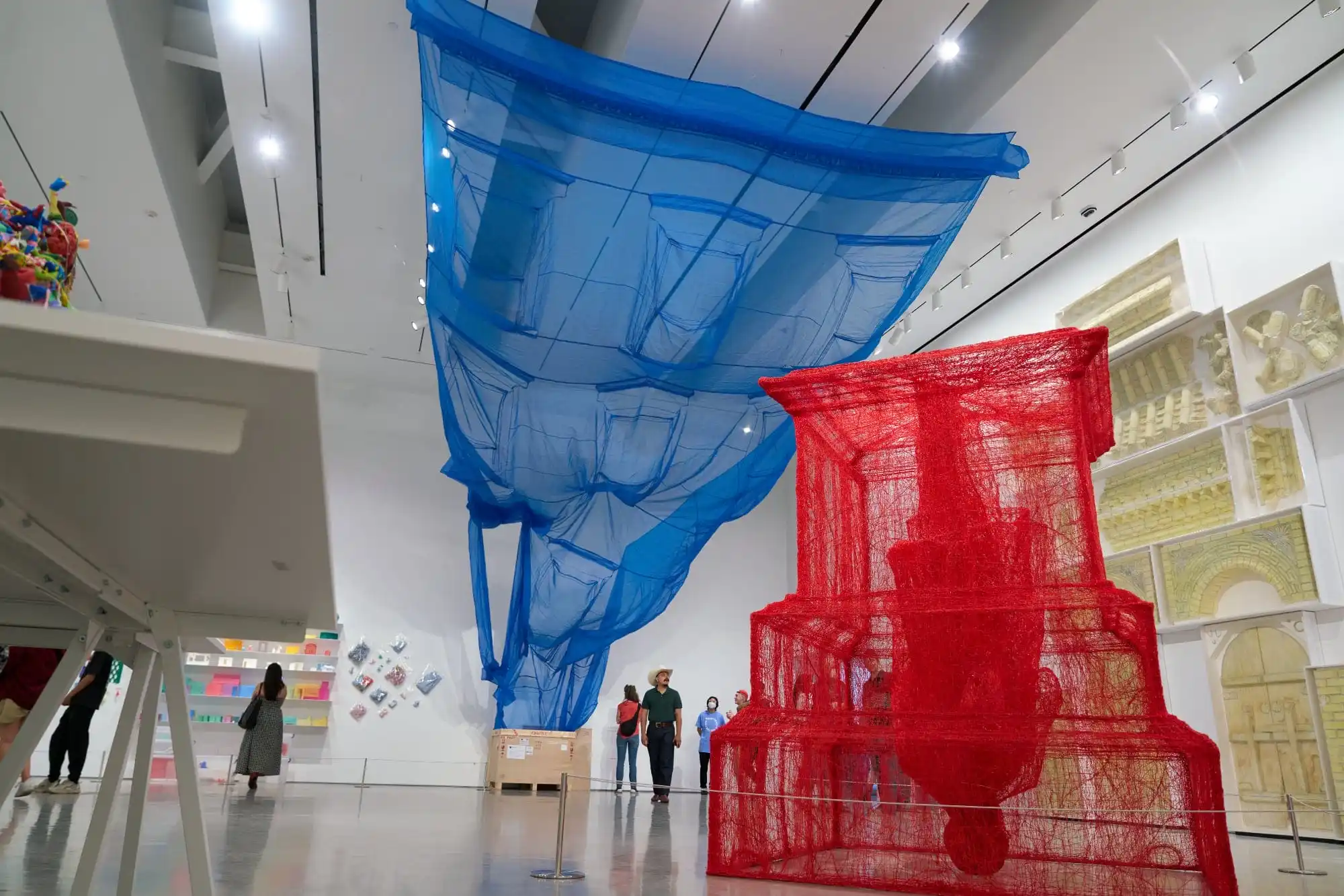 a massive blue fabric suspends from the ceiling while a red string covered structure stands in the gallery