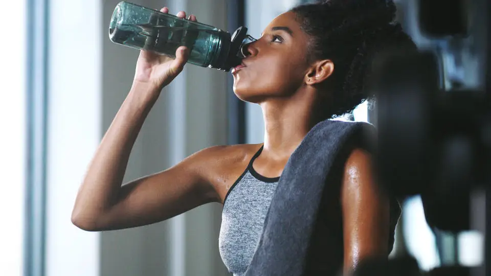 A woman drinking from her water bottle at the gym