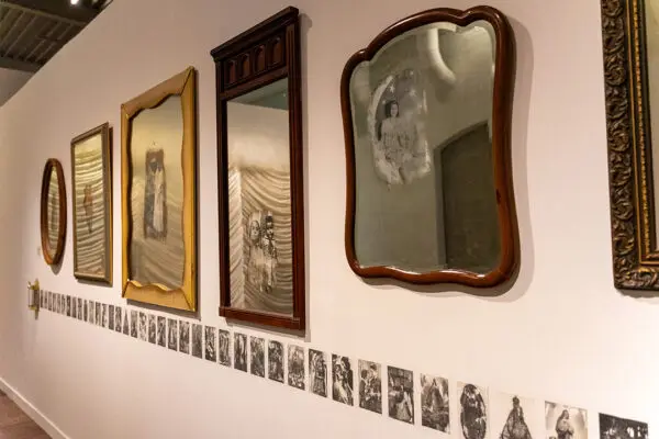 An installation image of an array of mirrors hung on a wall with images peering through the mirrored back.