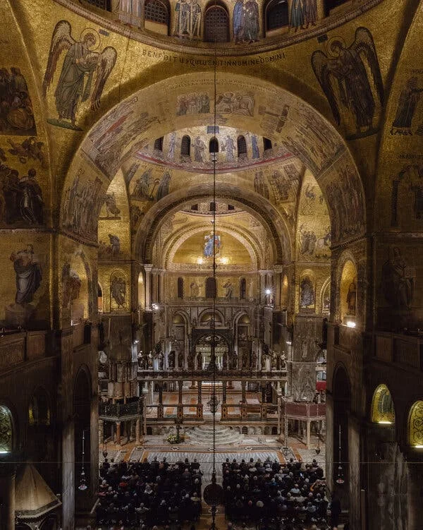 An interior view of the gilded, ornately decorated St. Mark’s Basilica, with people seated to attend a performance.