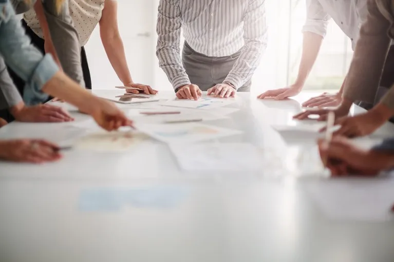 Low angle view of hands of a group of people working together around a table of paper documents.