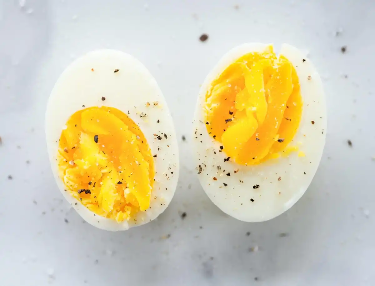 Two halves of a hard-boiled egg sprinkled with pepper on a white surface.