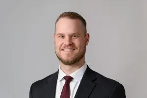 Nick Kuhlman, wearing a tie and suit jacket, smiles at the camera