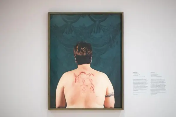 A multimedia piece featuring a model's bare back, with various illustrations carved into it.