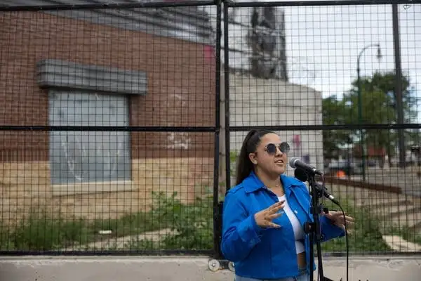 A woman speaks into a mic outside a fence