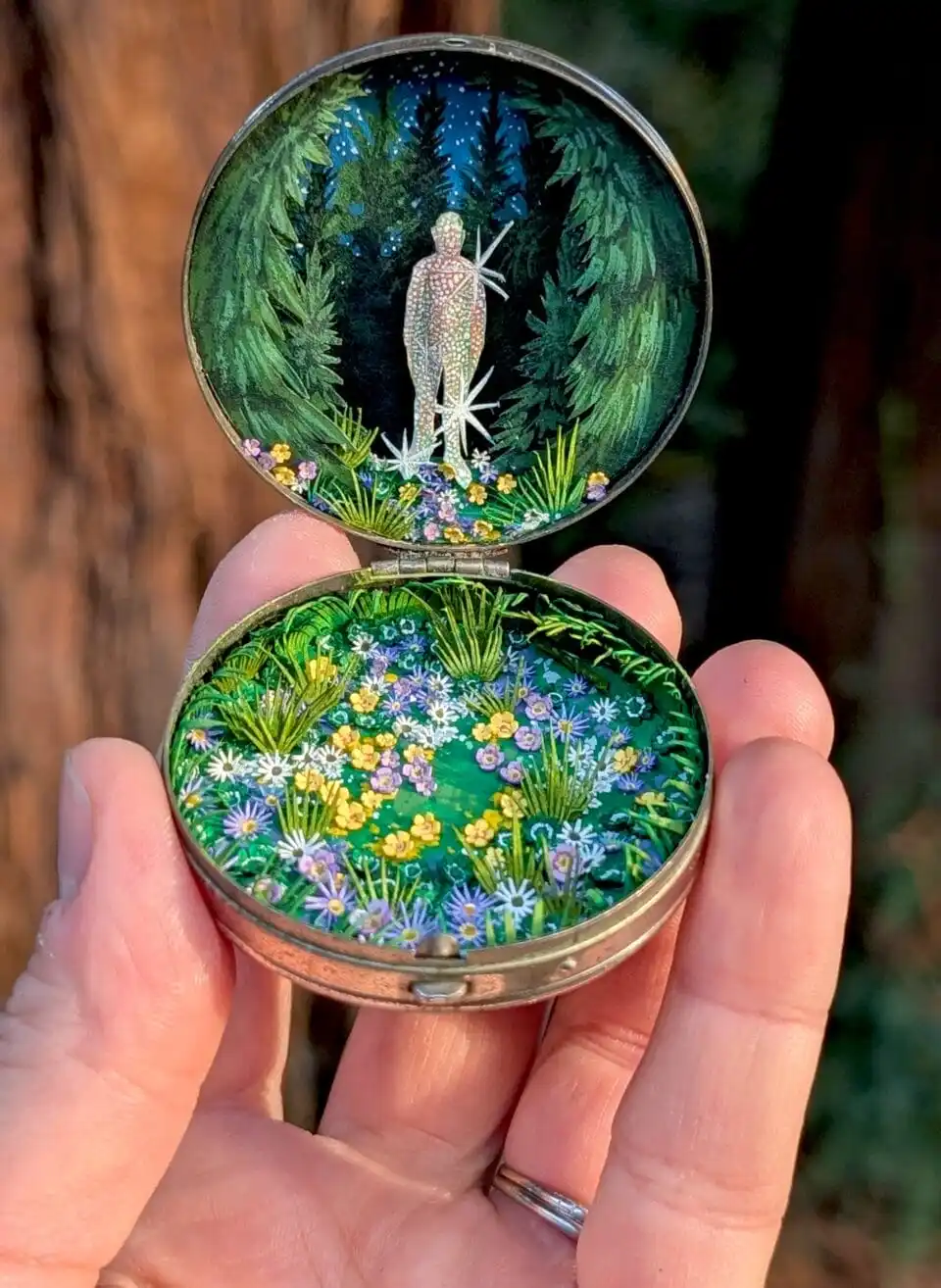 a watercolor pond with lush plants and lily pads is nested inside an antique compact. an obscured figure is on the upper part