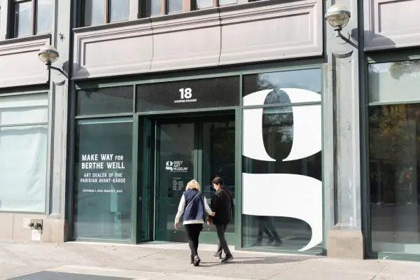 Two women can say two women entering the Grey Art Museum. The lettering on the window reads “Make Way For Berthe Weill” and “Art Dealer of the Parisian Avant-Garde.” The door reads “Grey Art Museum.”