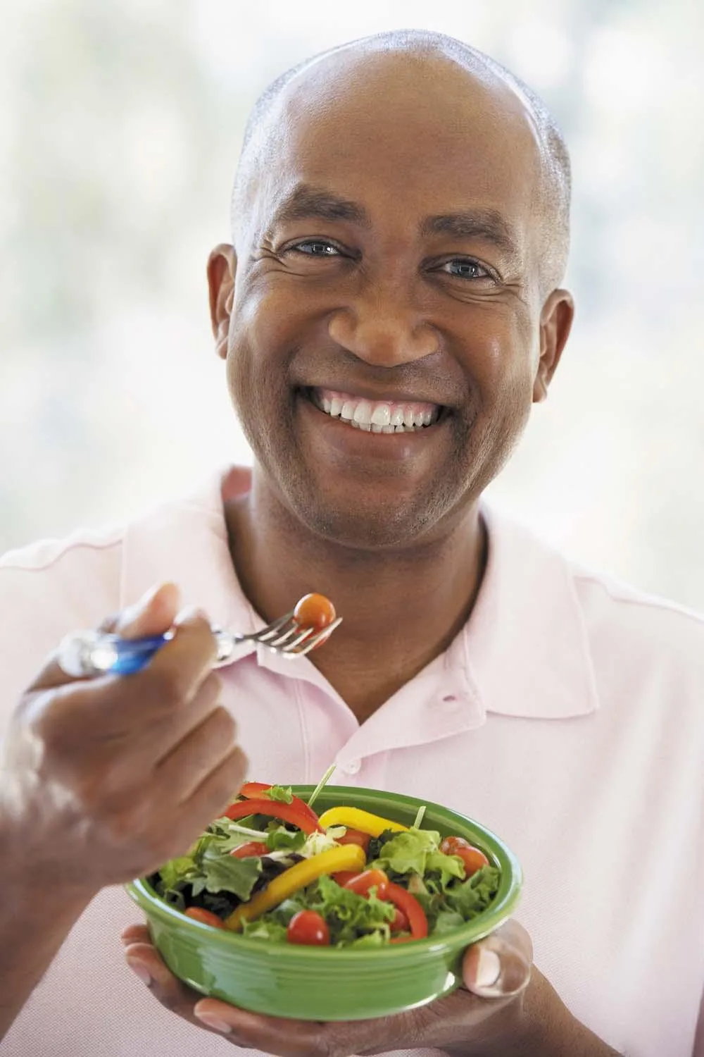 A smiling man holds a bowl of fresh fruit and a fork.