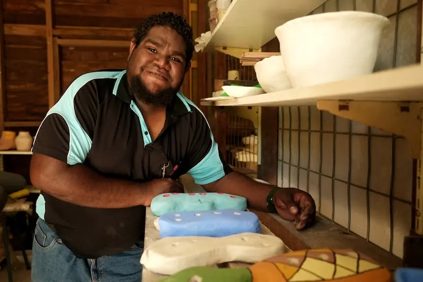 An Aboriginal man smiles while working in a ceramic workshop.