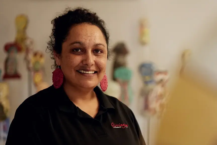 A smiling woman standing in art gallery with ceramic figures behind her.